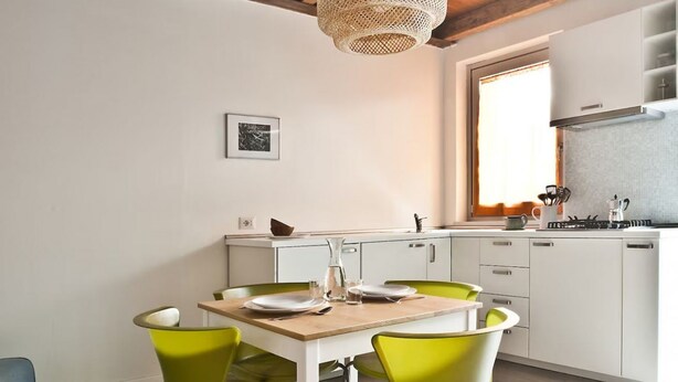 Una cocina moderna con armarios blancos, una mesa de madera y sillas verdes.