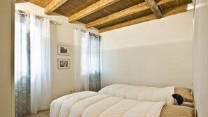 Un dormitorio con techo de madera, una cama con ropa blanca y dos cuadros en la pared.