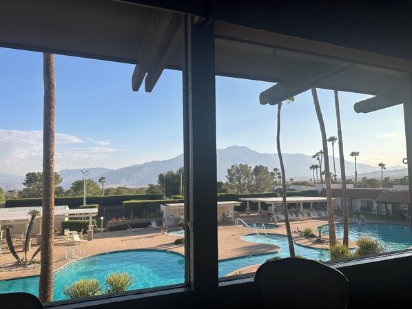 A view of a swimming pool area with multiple pools, palm trees, and a mountain backdrop.