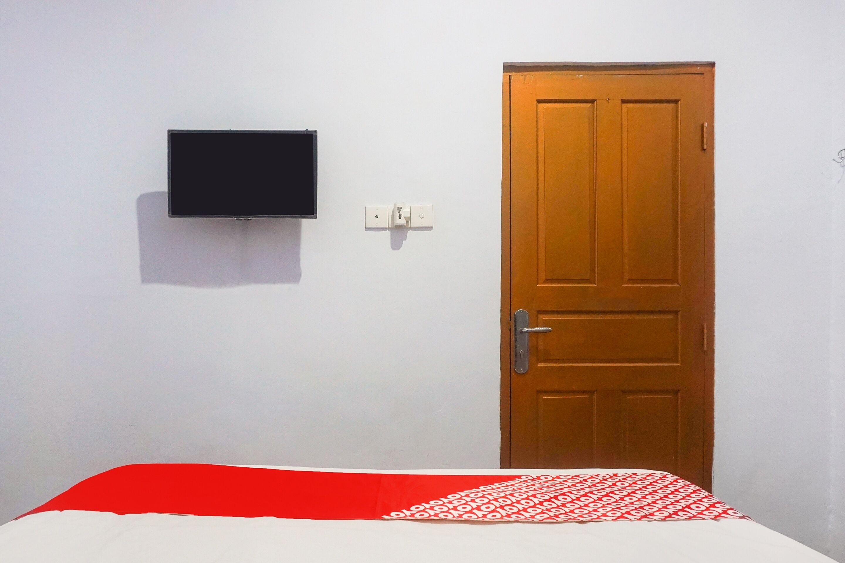 Een kamer met een bed, een houten deur en een tv aan de muur.