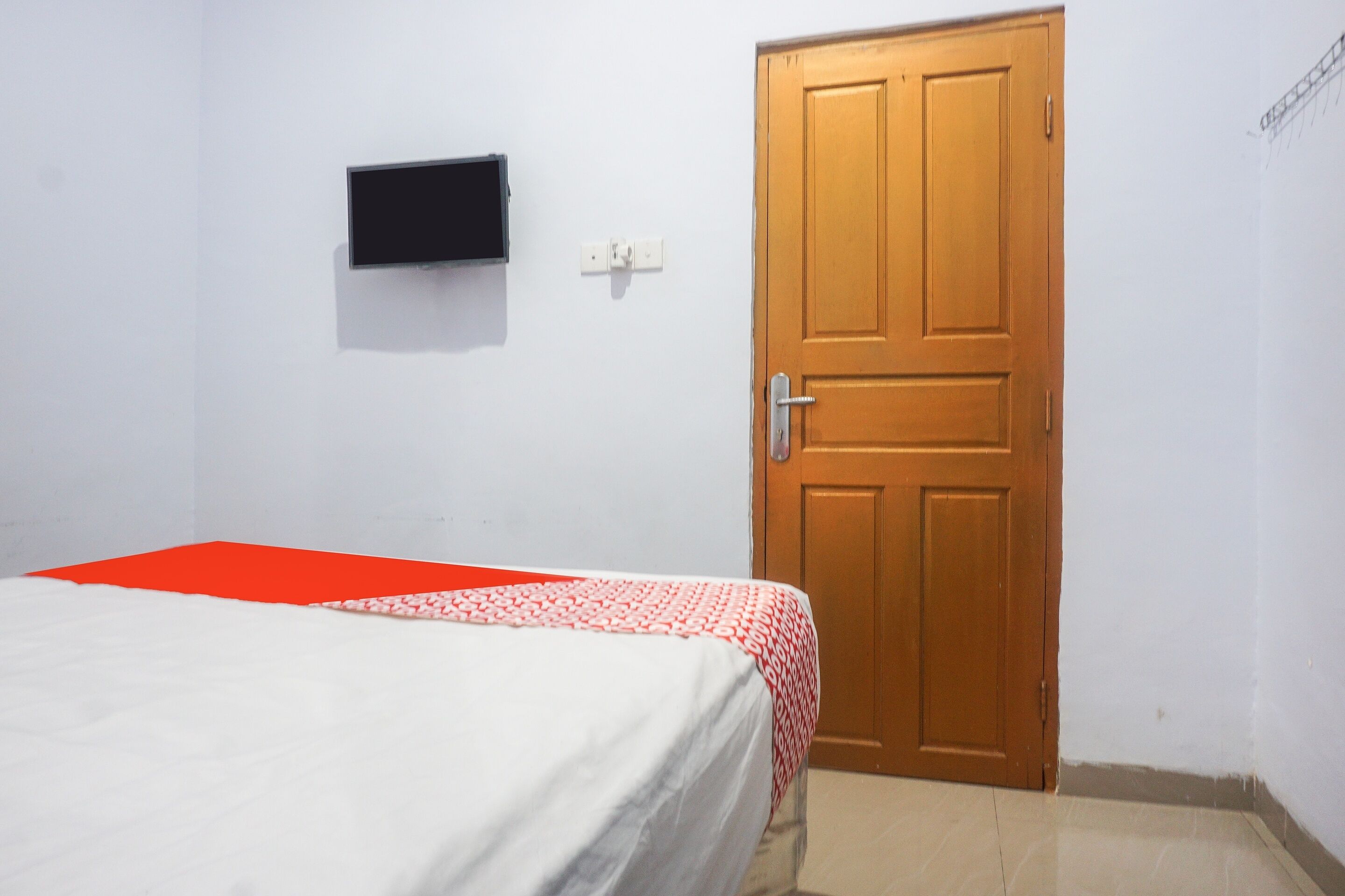 A room with a bed, a wooden door, a wall-mounted TV, and a power outlet.