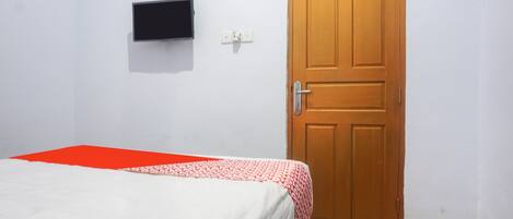 A room with a bed, a wooden door, a wall-mounted TV, and a power outlet.