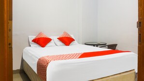 Ein Hotelzimmer mit einem Bett, zwei roten Kissen, einer weißen Bettdecke und einem kleinen runden Tisch mit einem Stuhl.
