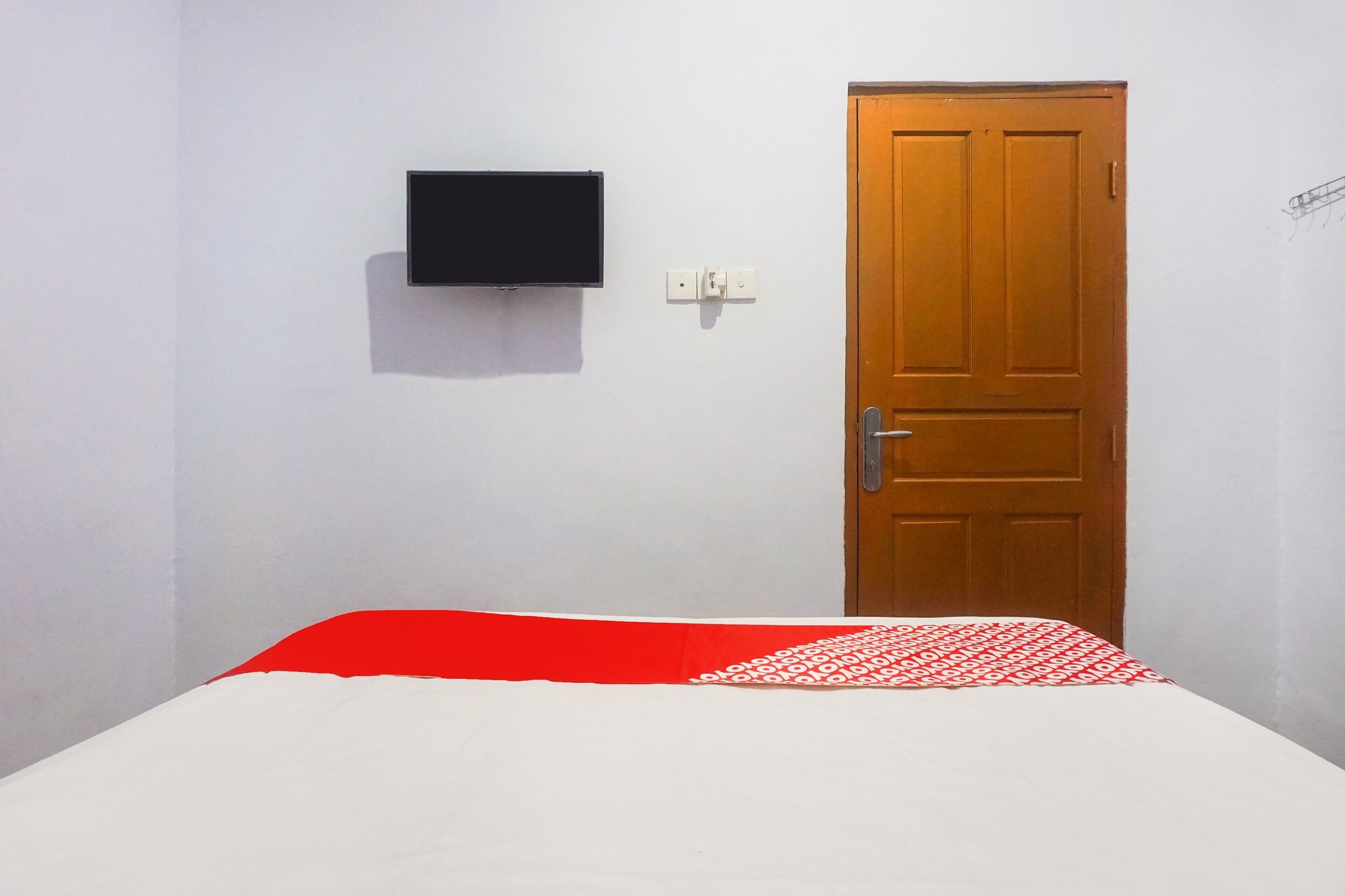 Une pièce avec un lit, une porte en bois et un téléviseur fixé au mur.