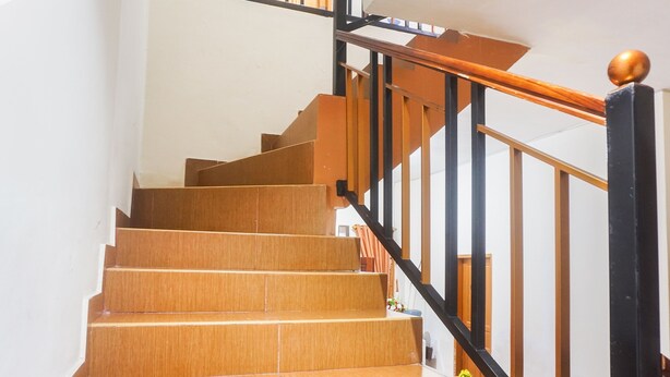Eine Holztreppe mit schwarzen Geländern und einem Holgitter auf der rechten Seite.