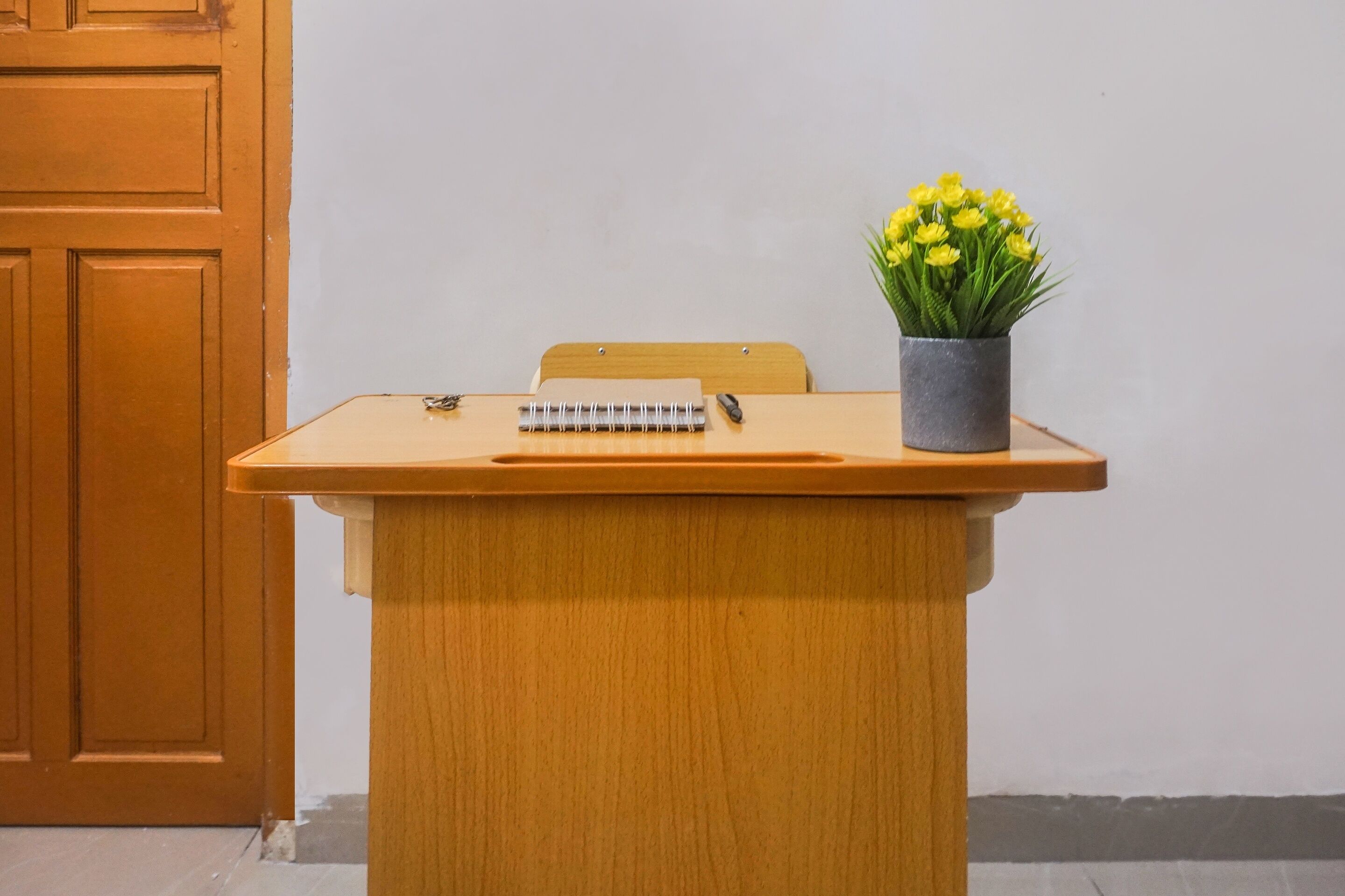Un bureau en bois avec un carnet à spirale, un stylo et une plante en pot.