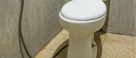 A toilet with a handheld showerhead in a bathroom with tiled walls and floor.