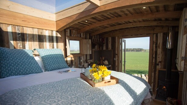 A cozy bedroom with a bed, a wooden ceiling, and a view of the outdoors. - The Sanderling  - sleeps 2 guests  in 1 bedroom (Beadnell)