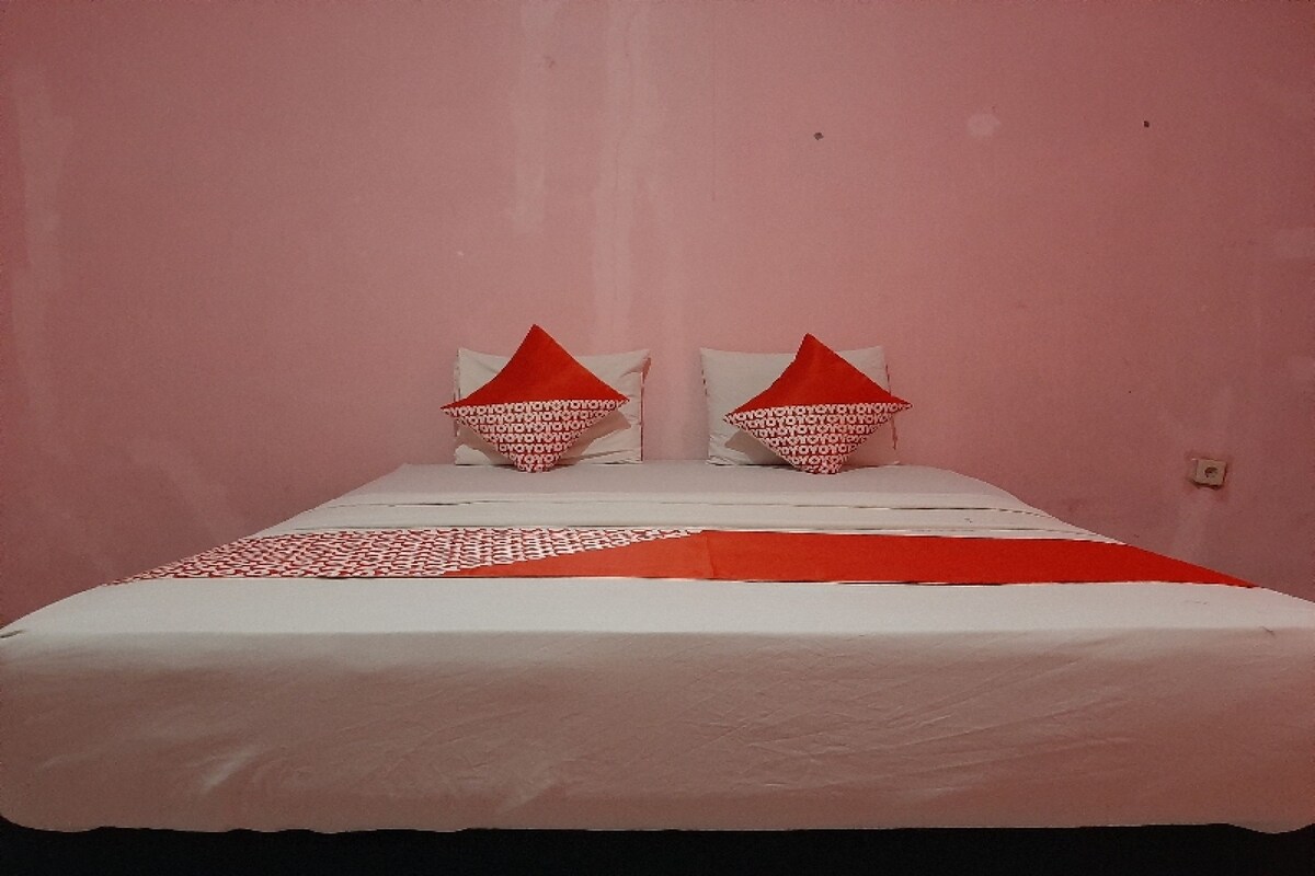 Un lit avec une literie blanche et des oreillers rouges, placé devant un mur rose.