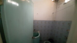 A small, dimly lit bathroom with a single toilet, a sink, and a wall with a patterned tile design. - OYO 90555 Vina Pavilion (Bengkulu)