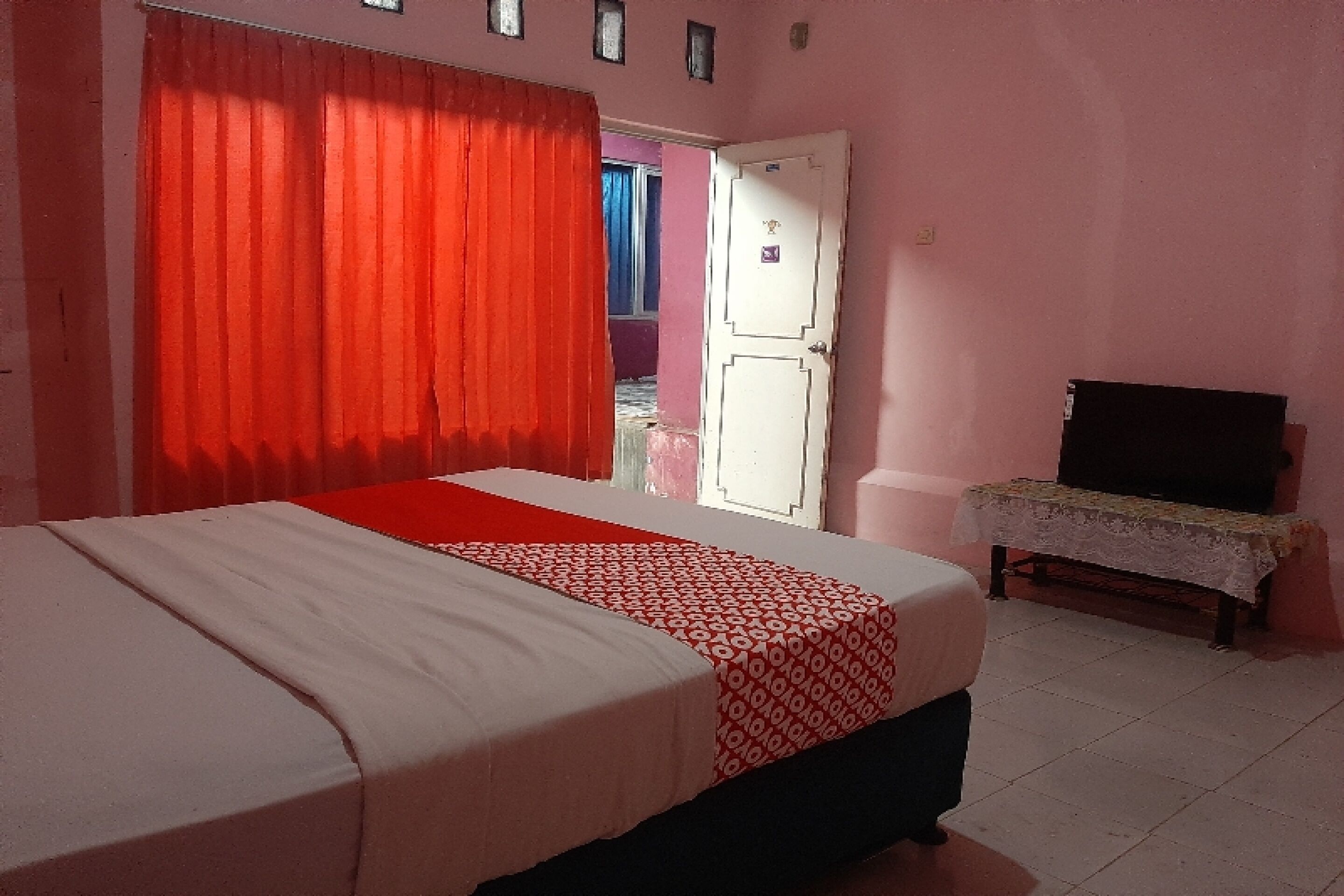 A bedroom with a bed, a television on a stand, and a door leading to another room.