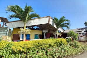 A building with a covered entrance, palm trees, and a well-maintained garden with various plants and flowers.