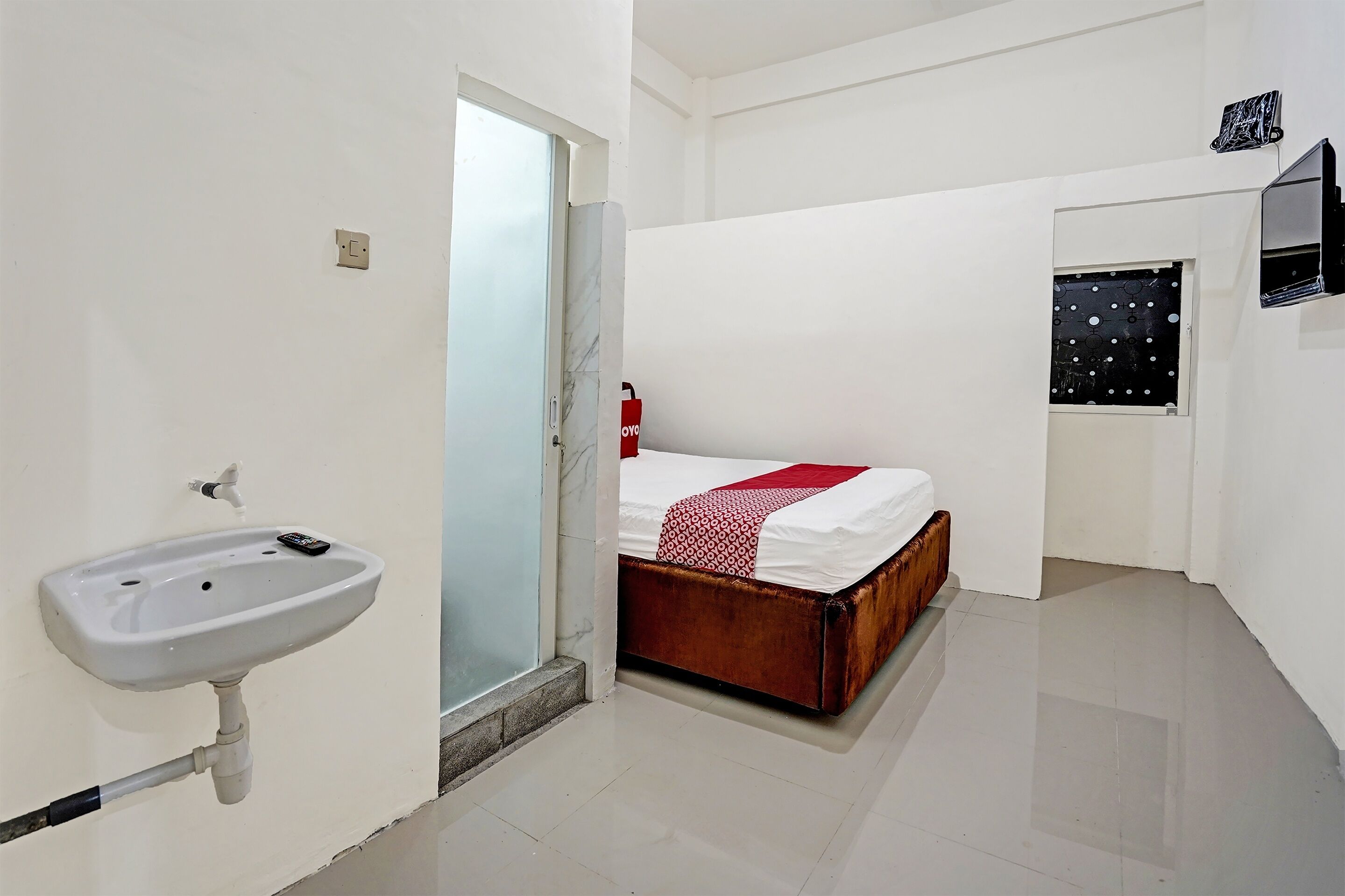 Une chambre à coucher comprenant un lit, une table de chevet, un téléviseur fixé au mur et une fenêtre avec un rideau.