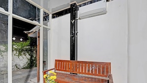 A wooden bench with a white vase of yellow flowers, a tiled floor, and a large window with a view of greenery. - Hotel O Grand Syariah Hagawa Lamongan Near SPORT CENTER LAMONGAN (Lamongan)