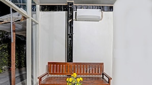 A wooden bench with a white table in front, a potted plant with yellow flowers, and an air conditioning unit mounted on the wall. - Hotel O Grand Syariah Hagawa Lamongan Near SPORT CENTER LAMONGAN (Lamongan)