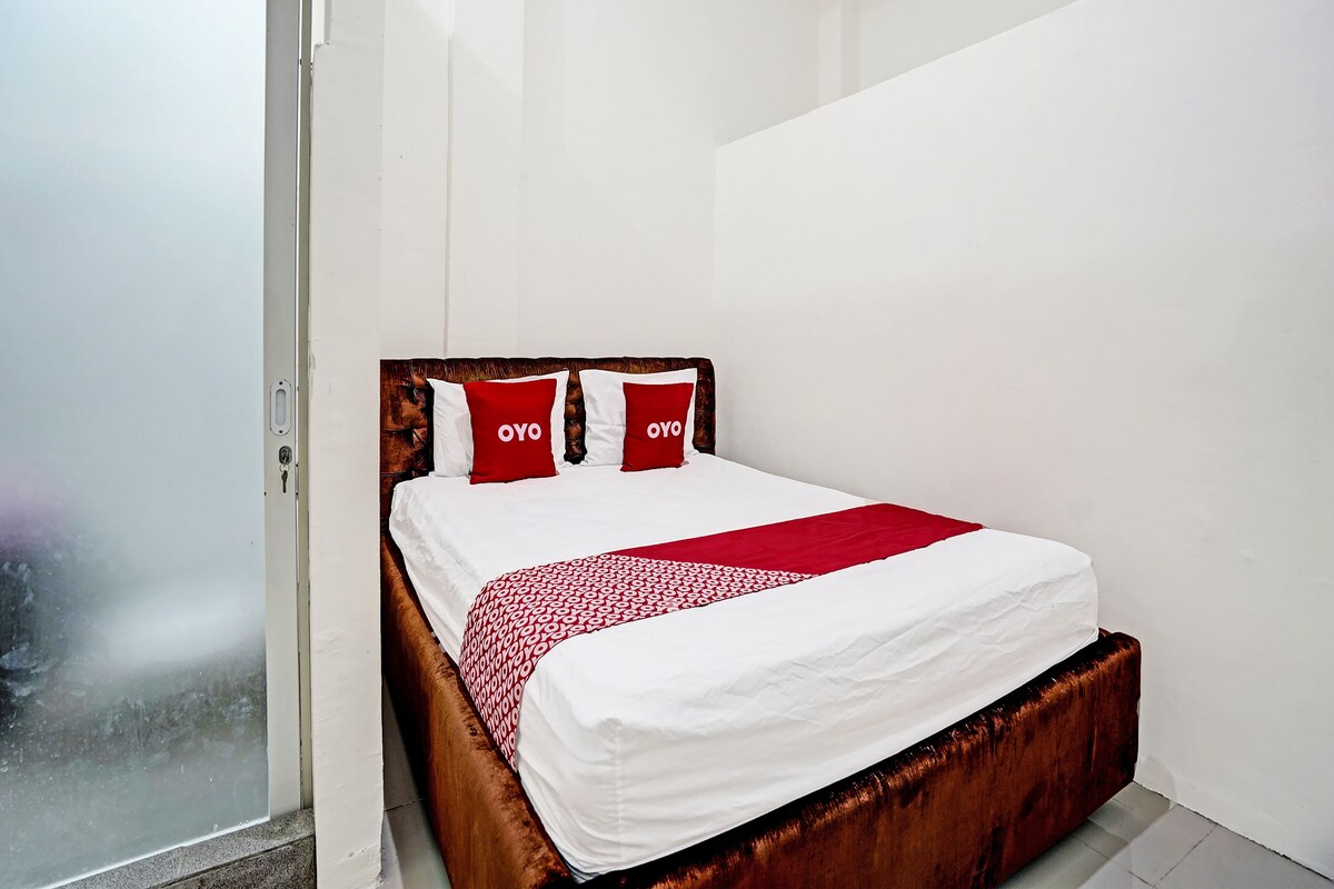A single bed with a wooden headboard, white bedding, and two red pillows with "OYO" text.