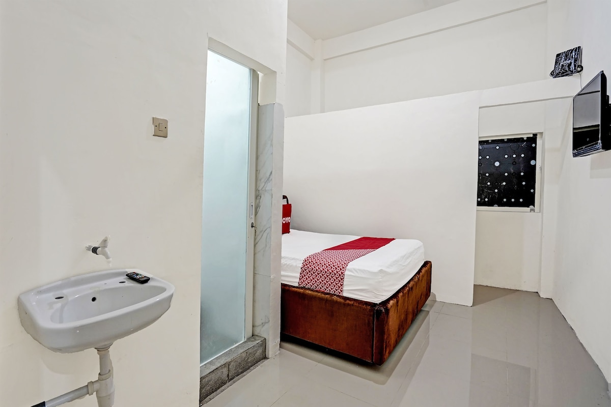 A hotel room with a bed, a bedside table, a mirror, and a bathroom with a sink and toilet.