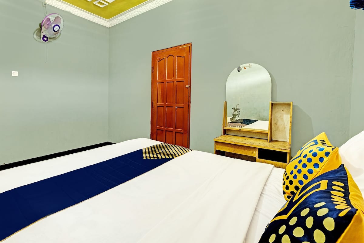 Un dormitorio con una cama, una puerta de madera, un espejo y una mesita.