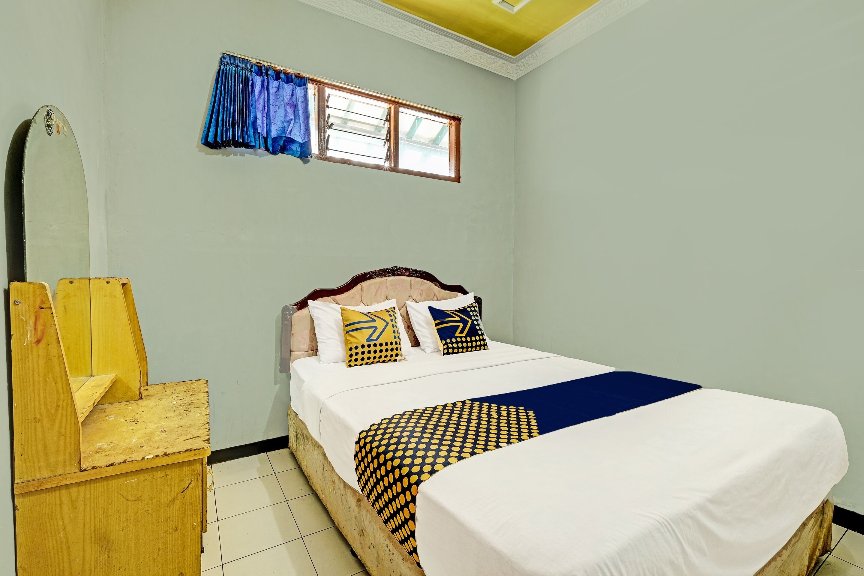 A bedroom with a bed, a wooden nightstand, a window with curtains, and a ceiling light fixture.