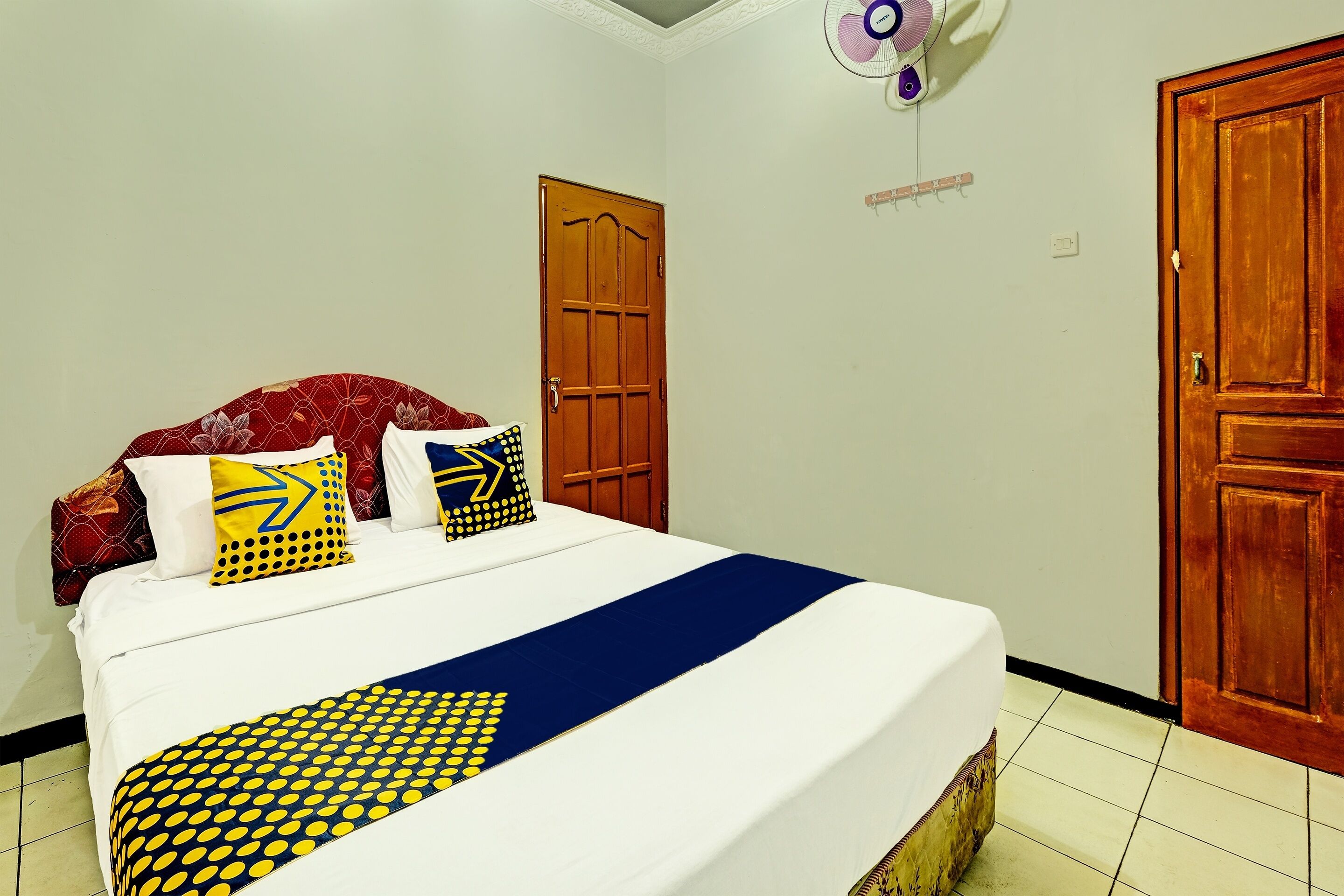 A neatly made bed with a blue and yellow patterned bedspread, a white pillow with a yellow arrow design, and a red pillow with a floral pattern.
