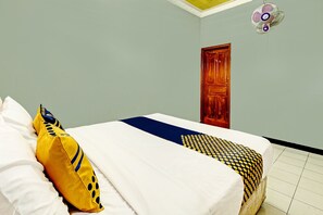 Una cama bien hecha con ropa de cama blanca y estampada, una puerta de madera y un ventilador de techo.