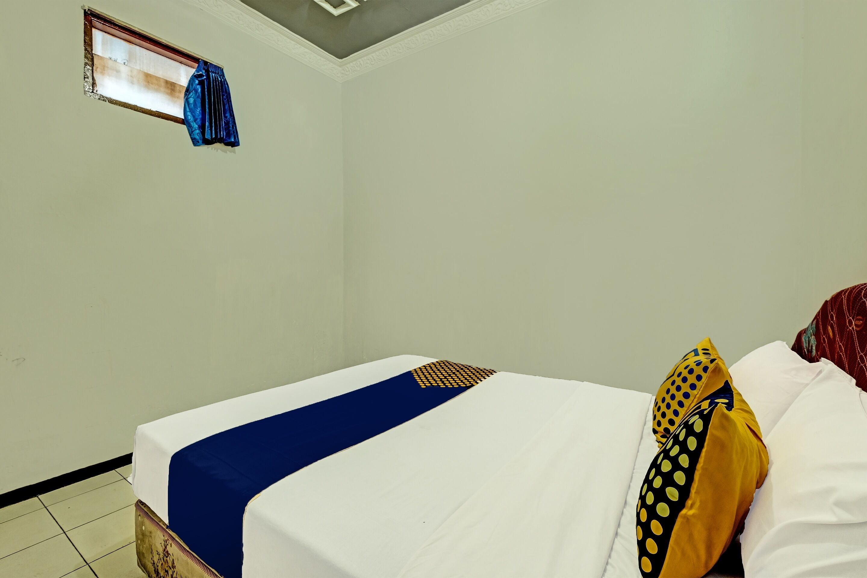 A hotel room with a bed, a window with a curtain, and a tiled floor.