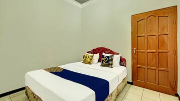 A neatly made bed with a white and blue bedspread, two pillows with geometric patterns, and a wooden door to the right.