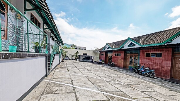A courtyard with stone flooring, a green metal railing, and a red building with a tiled roof. - SPOT ON 91715 Hotel Citra Dewi 1 (Bandungan)