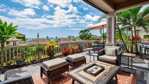 Eine überdachte Terrasse im Freien mit Rattanmöbeln, einem Grill und Blick auf den Ozean.