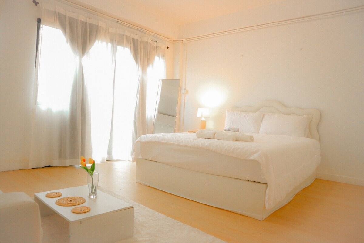 A minimalist bedroom with a large bed, a bedside table, and a mirror.