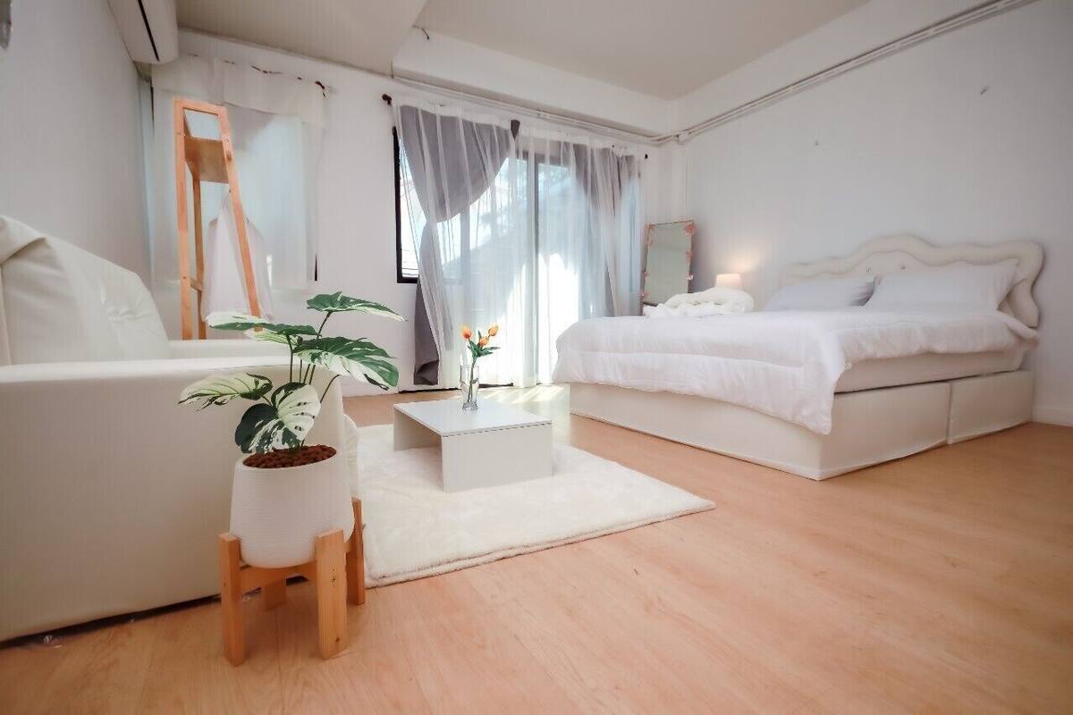 A minimalist bedroom with a bed, a white sofa, a small table with a plant, and a mirror.