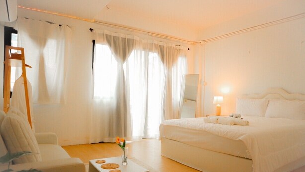 A hotel room with a large bed, a bedside table with a lamp, a chair, and a small table with a vase of flowers. - HaneulHotelChiamai (Chiang Mai)