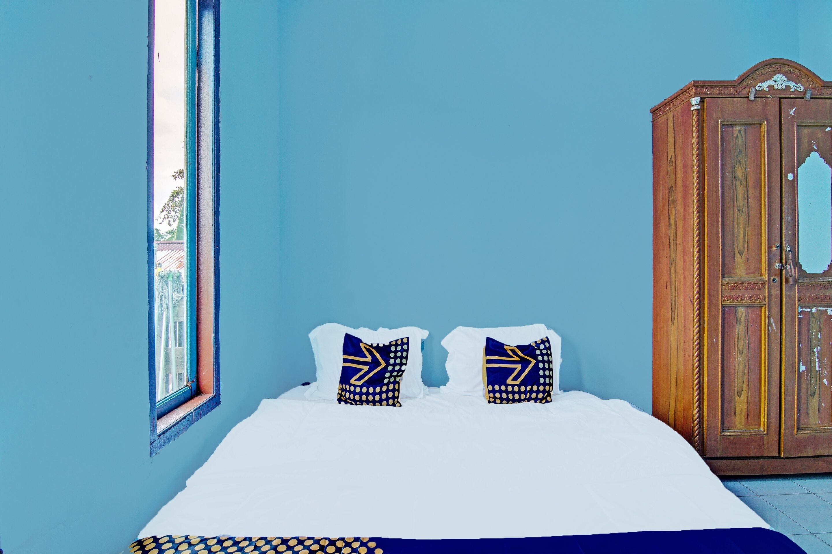 A bedroom with a bed, two pillows, a wardrobe, and a window.