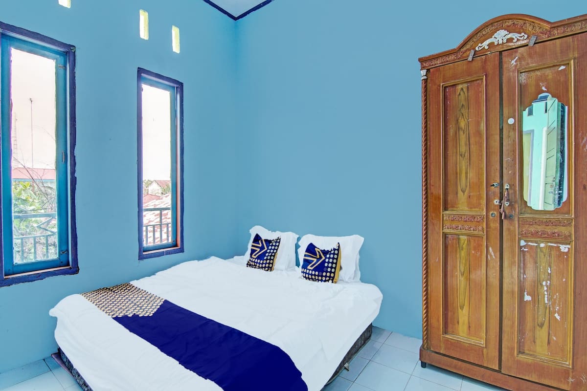 Un dormitorio con cama, dos ventanas, un armario y vistas al balcón.