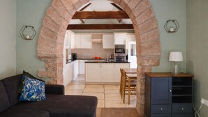 A living room with a sofa, a coffee table, and a TV. There is a kitchen visible through an archway with white cabinets and a microwave. - A cottage that sleeps 2 guests  in 1 bedroom (Longtown)