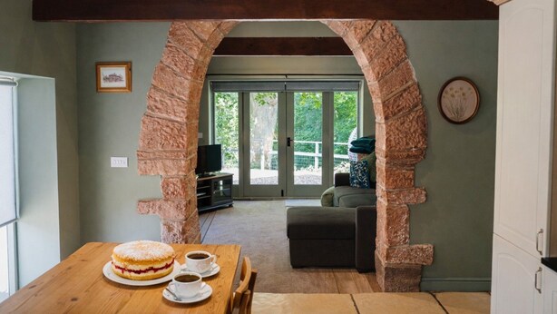 A dining area with a stone archway, a table with a dessert and coffee, and a view of the outdoors. - A cottage that sleeps 2 guests  in 1 bedroom (Longtown)