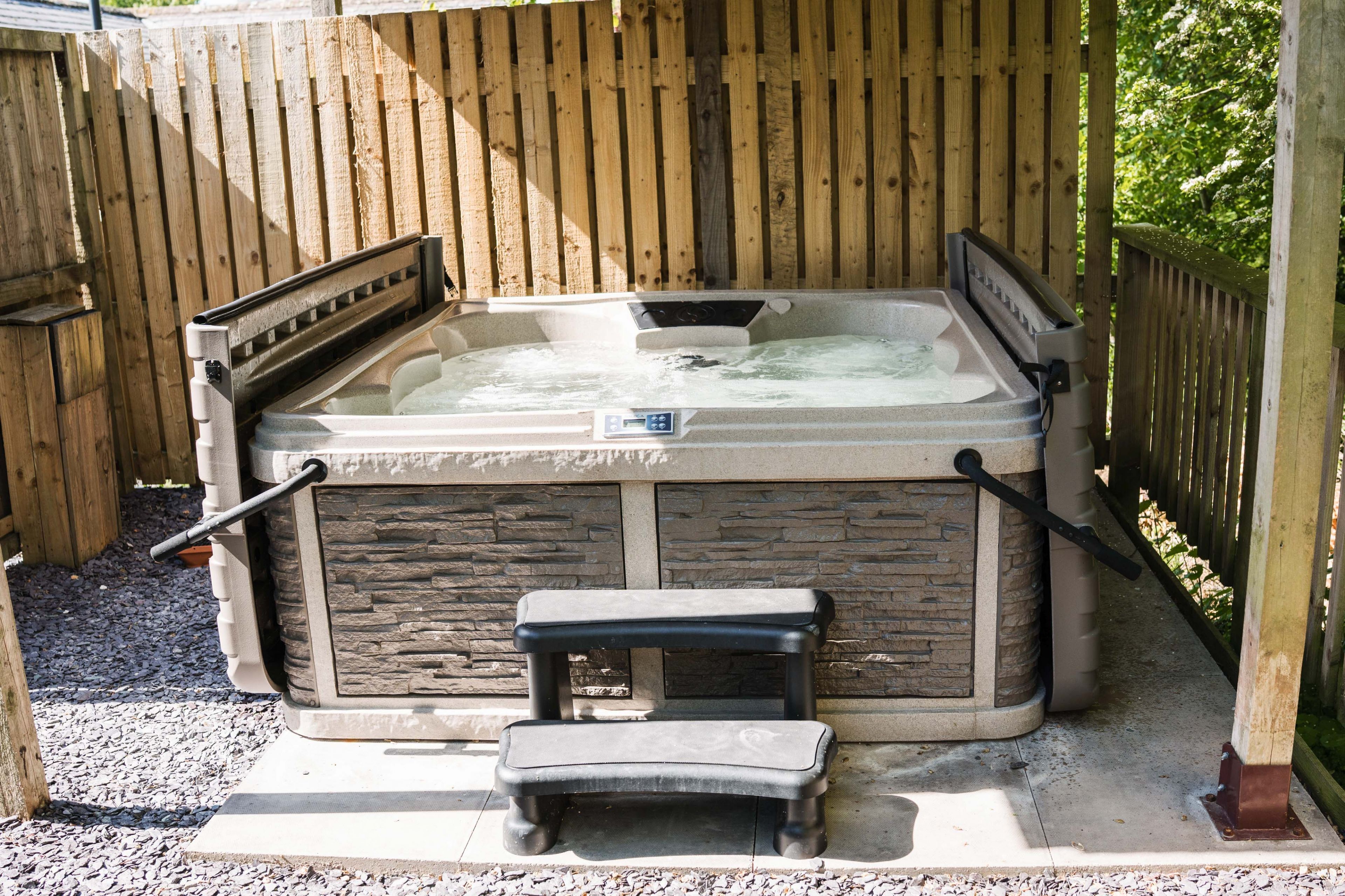 Un jacuzzi con revestimiento de piedra, una terraza de madera y un pequeño banco.