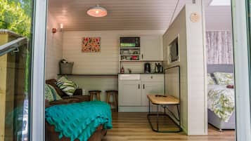 Een gezellige kamer met een bed, een klein keukentje, een eettafel en een raam met uitzicht op groen.
