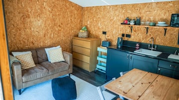 Un espace de vie compact comprenant un coin cuisine, un canapé, une table en bois et un petit tapis.