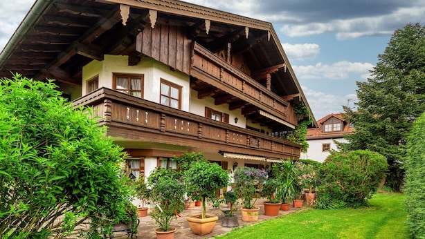 A traditional chalet with a wooden balcony, multiple windows, and a garden with potted plants.