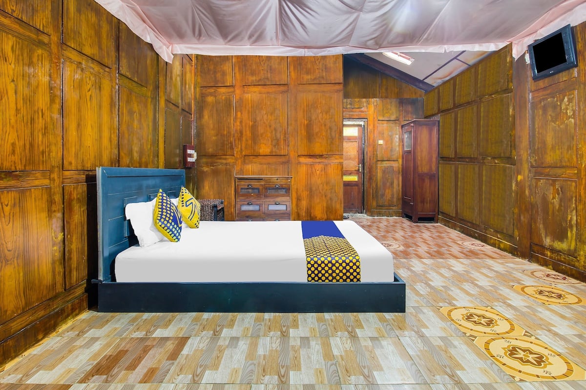 Una habitación con una cama, paneles de madera, suelo estampado y un televisor.