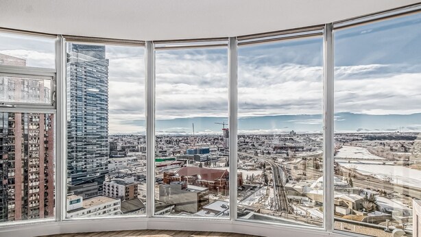 Panoramisch uitzicht vanuit een hooggelegen kamer met grote ramen, waarop een stadsgezicht met verschillende gebouwen en infrastructuur te zien is.