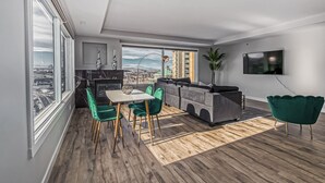 Een moderne woonkamer met een eethoek, grote ramen, een televisie en uitzicht over de stad.