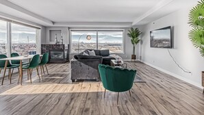 Een moderne woonkamer met een groot raam, een grijze bank, een eettafel met stoelen en een stadsgezicht.