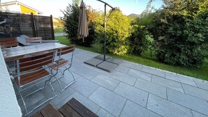 Een terras buiten met een tafel en stoelen, een pergola met een overkapping en uitzicht op een groen landschap.