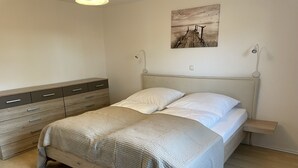 Een slaapkamer met een houten bed, een nachtkastje, een dressoir en een wandlamp.