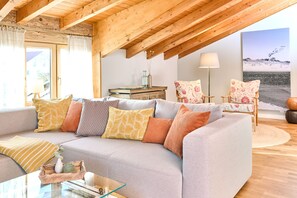 Una sala de estar acogedora con un sofá gris, cojines estampados, una mesa de centro de cristal y techo de madera.
