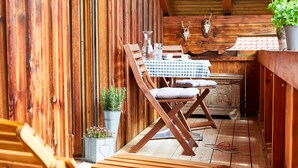 Een houten eethoek buiten met een geruit tafelkleed, houten stoelen en een rustieke inrichting, waaronder een herten schedel en potplanten.