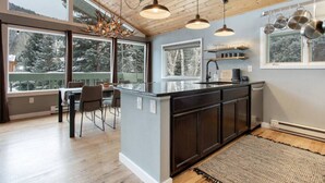 A modern kitchen with a large island, pendant lights, and a view of snowy trees through large windows.