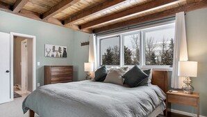 A bedroom with a bed, nightstands, a window with a view of trees, and a wooden ceiling.
